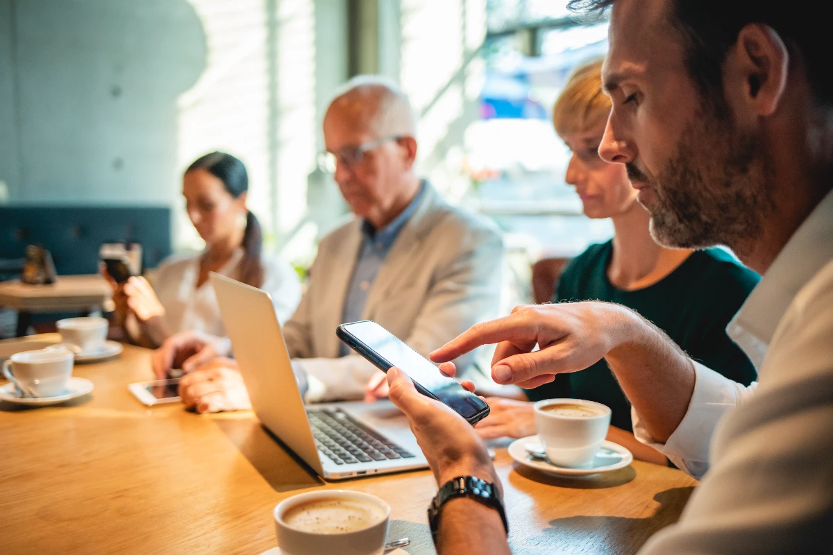 Coworkers with coffee using their mobile devices in a coffeeshop instead of a meeting room